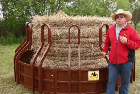 A big cattle and horse hay feeder with a cowboy next to it.