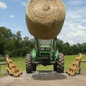 large tractor crossing concrete cattle guard with huge hay bale