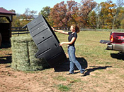 hay feeder being lowered over a large round hay bale